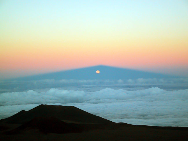 La luna sale a través de la sombra del Mauna Kea